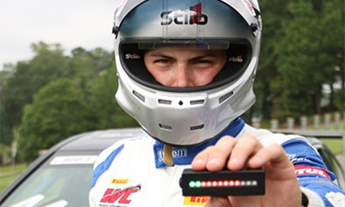 Andrew Rains in driving gear holding up his patented device that measures a car's acceleration and deceleration patterns