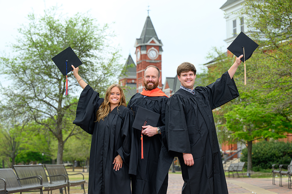 3 people in cap and gown on Auburn campus