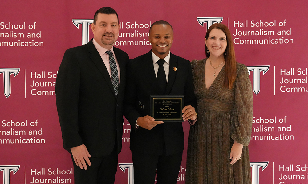 3 people standing together with award