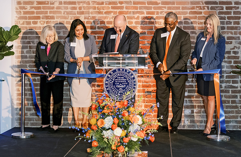 Five people cutting ribbon in building