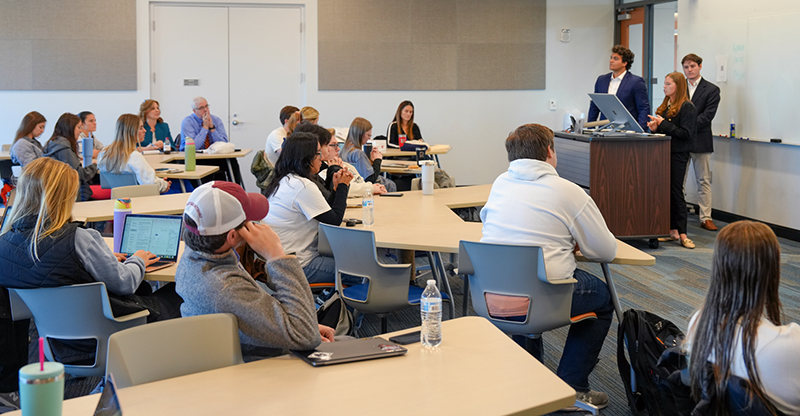 4 students speaking to class of students