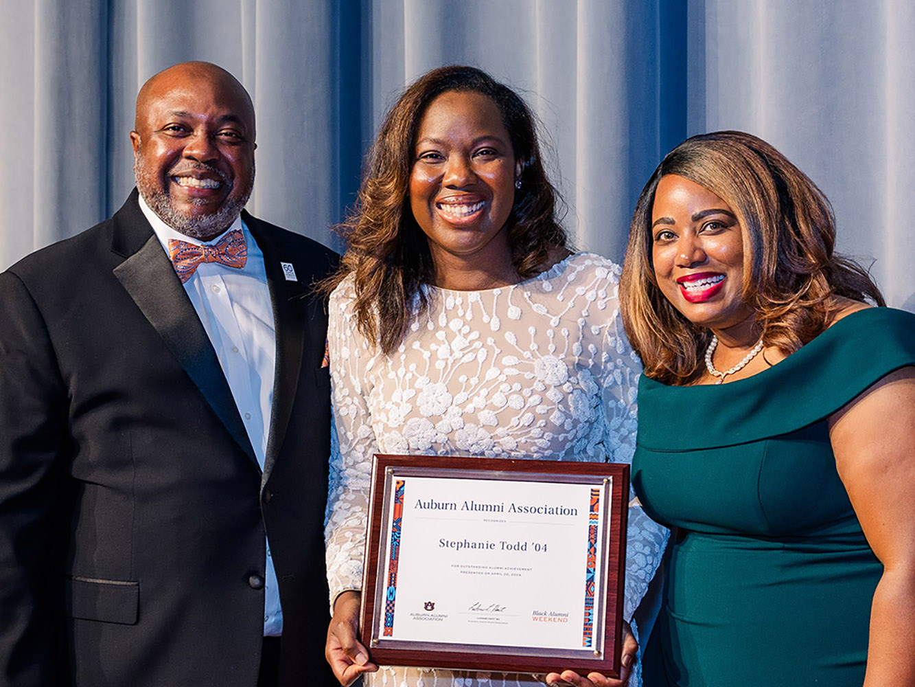 Award winner holding plaque with 2 other people.
